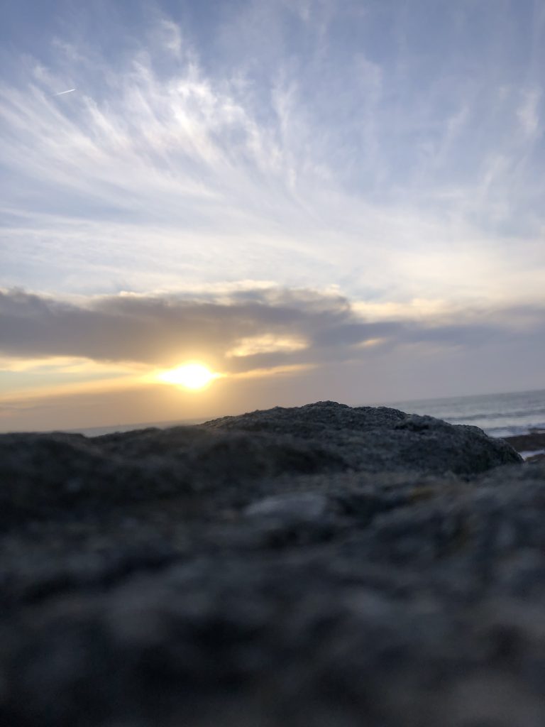 Sunrise over a rocky coastline with soft clouds and golden light at the horizon.